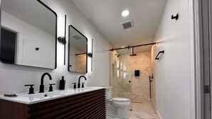 A modern bathroom with a vanity, two mirrors, a shower, and a toilet. - Charming 3-bedroom house in Tamarac. Minutes from Hardrock, Beaches, & Shopping (Tamarac)