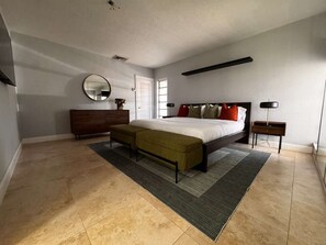 Ein Schlafzimmer mit einem Bett, einer Bank, einem Schminktisch, einem Spiegel und einem Nachttisch.