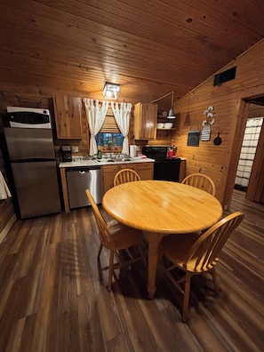 A wooden interior with a kitchen, dining table, chairs, and a refrigerator.