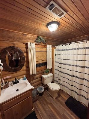 Ein Badezimmer einer HolzhĂŒtte mit Waschbecken, Toilette und Duschvorhang.