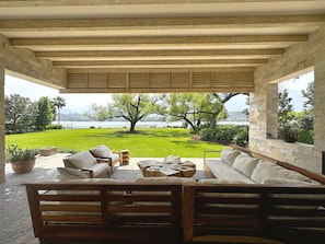 Une terrasse extérieure avec des meubles en bois, un mur en pierre et une vue sur un lac et des montagnes.