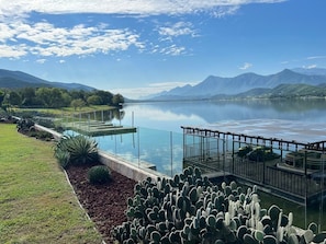 A lake with a dock, cacti, and mountains in the background.
