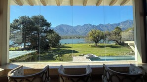A view from a room with a large window overlooking a lake, mountains, and a well-maintained lawn with a pool and seating area. - Unique Lakefront estate, Santiago NL minutes from Monterrey, villa la Boca (Santiago)