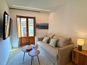 Ein modernes Wohnzimmer mit einer Couch, einem kleinen Tisch, einer Lampe und einem an der Wand montierten Fernseher.