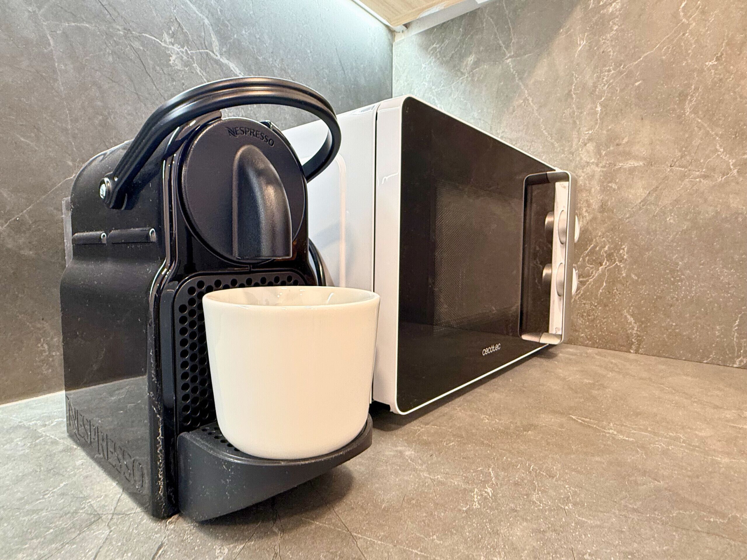 Eine Nespresso-Kaffeemaschine mit einer Tasse im Tropfenfänger, eine Mikrowelle und eine geflieste Spritzschutzwand.