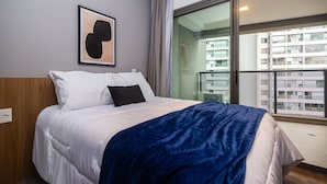 Habitación de hotel con cama, una obra de arte enmarcada en la pared y vistas a un balcón con edificios.