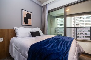 Een hotelkamer met een bed, een lijst met kunstwerk aan de muur en uitzicht op een balkon met gebouwen.