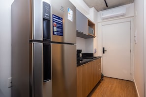 Eine kompakte Küche mit Edelstahl-Kühlschrank, Holzschränken, einer Kaffeemaschine und einer eingebauten Mikrowelle.