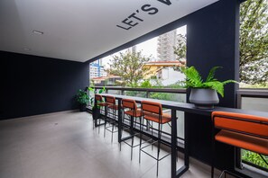 Uma varanda com uma fileira de banquetas, um vaso de planta e um letreiro com a inscrição 'LET'S VIBE'.