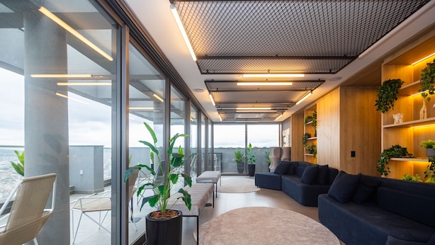 Un interior moderno con un gran ventanal, una zona de estar con sofá y sillones, y una planta en maceta.