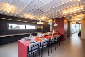 A modern kitchen with a red island, bar stools, and a view of the city through a window. - Studio no coração da Vila Madalena (São Paulo)