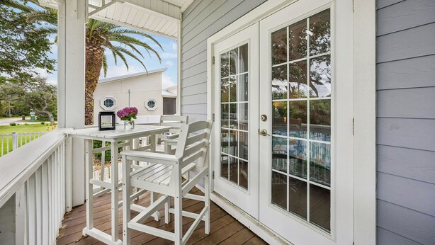 A covered porch with a white table and chairs, a door with glass panels, and a view of a house and palm tree. - Grand Floridian|Heated Pool|Walk to Beach|Sleeps 12 (St. Augustine)