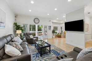 Uma sala de estar com sofá, poltrona, mesa de centro e televisão de tela plana na parede.