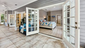 A spacious room with a large bed, a seating area with a sofa and chairs, and a glass door leading to an outdoor area. - Grand Floridian|Heated Pool|Walk to Beach|Sleeps 12 (St. Augustine)