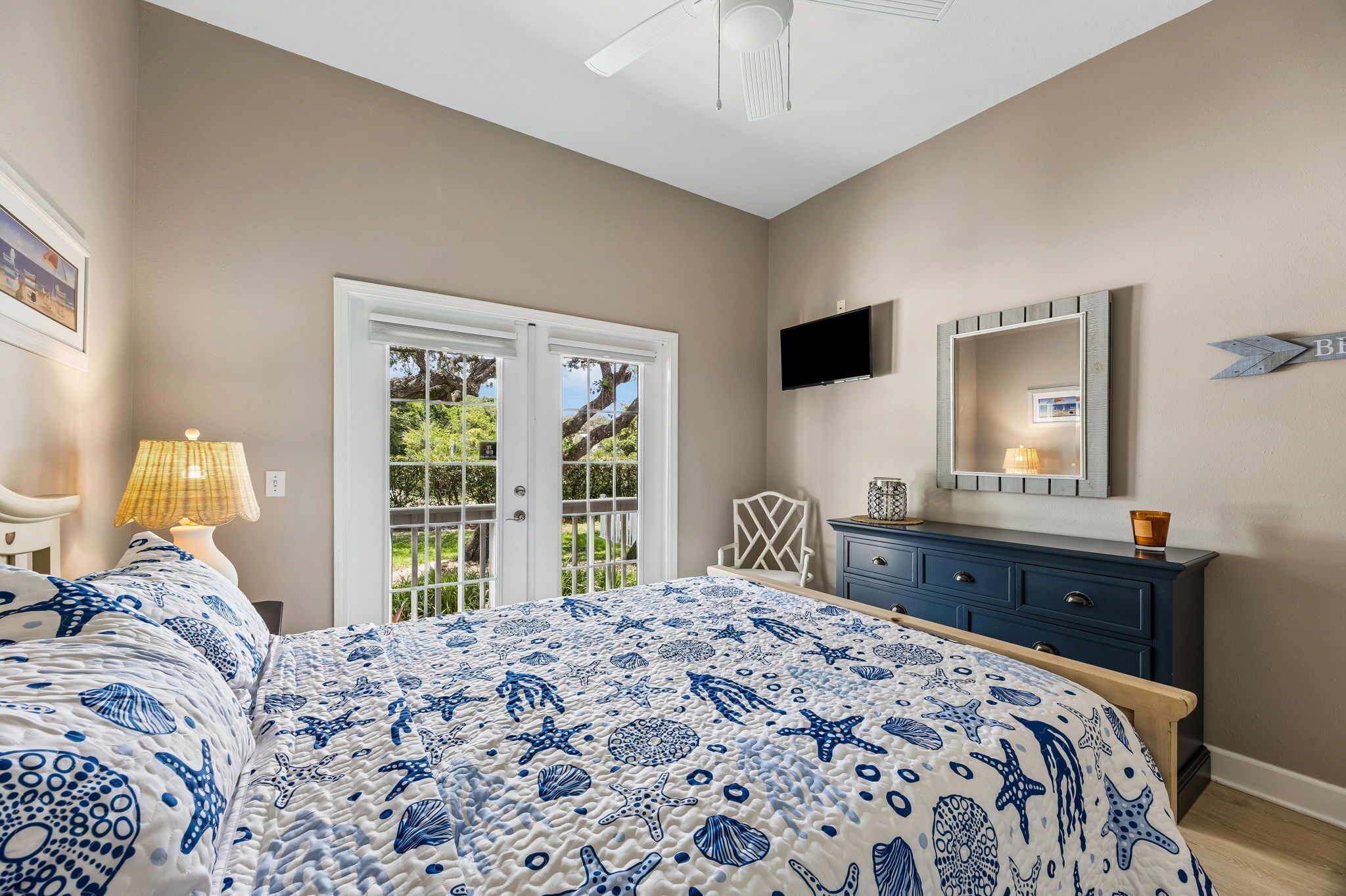 A bedroom with a bed, a dresser, a TV, and a door leading to a balcony.