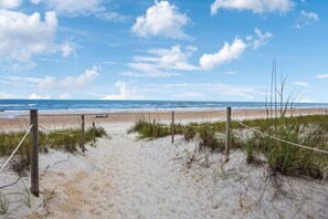 Uma trilha de areia que leva ao oceano, com uma barreira de corda e estacas de madeira.