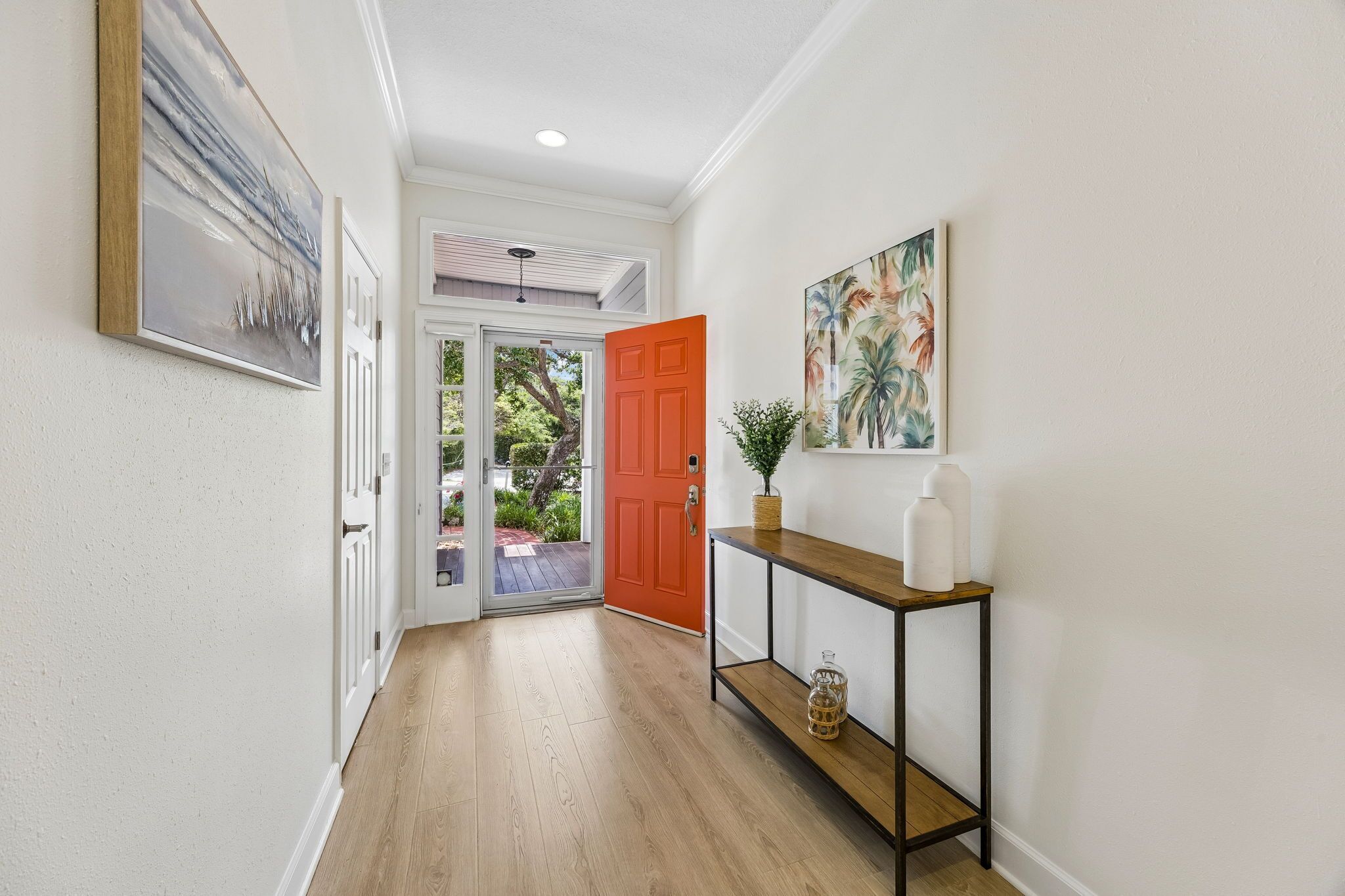 A hallway with a wooden floor, a red door, and a console table with decorative items.