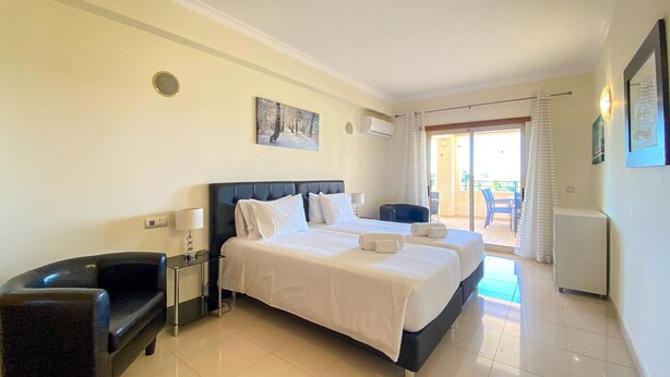 A hotel room with a large bed, a desk, a chair, a painting on the wall, and a balcony with a view. - Millennium Plaza by Hsrentals (Loulé)