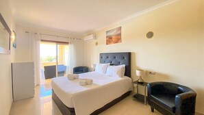 A hotel room with a large bed, a desk, a chair, and a balcony with curtains. - Millennium Plaza by Hsrentals (Loulé)