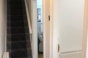 A narrow hallway with a carpeted staircase leading to a room with a bed and a radiator.