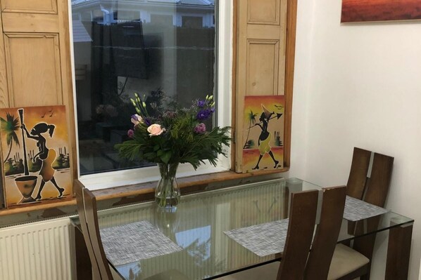 Un coin repas avec une table en verre, des chaises et un vase rempli de fleurs.