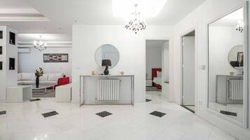 Habitación de hotel moderna con suelo de baldosas blancas y negras, una consola central con espejo, una araña y un sofá rojo, además de un espejo grande en la pared.