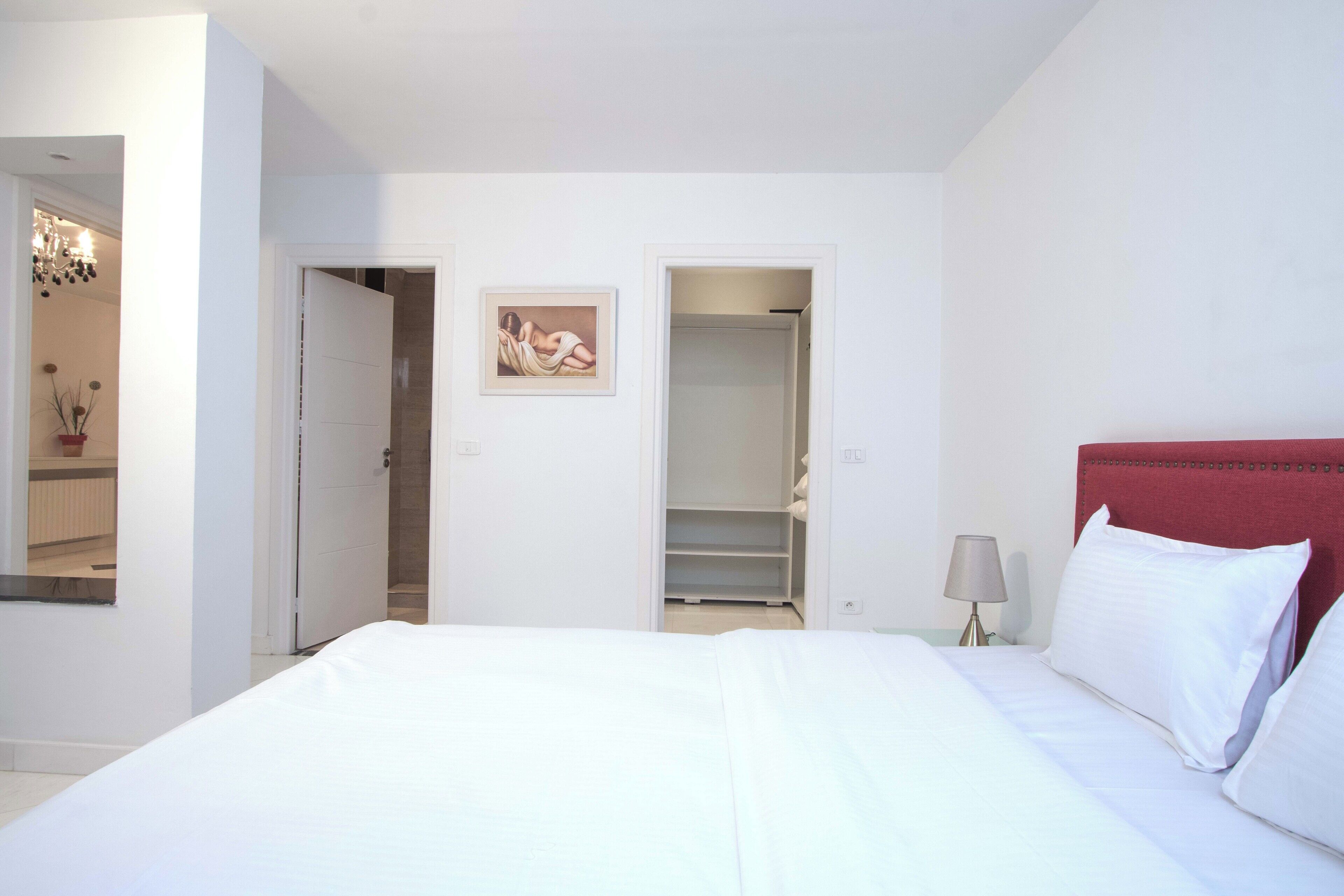 A hotel room with a large bed, a red headboard, a bedside table with a lamp, and a painting on the wall.