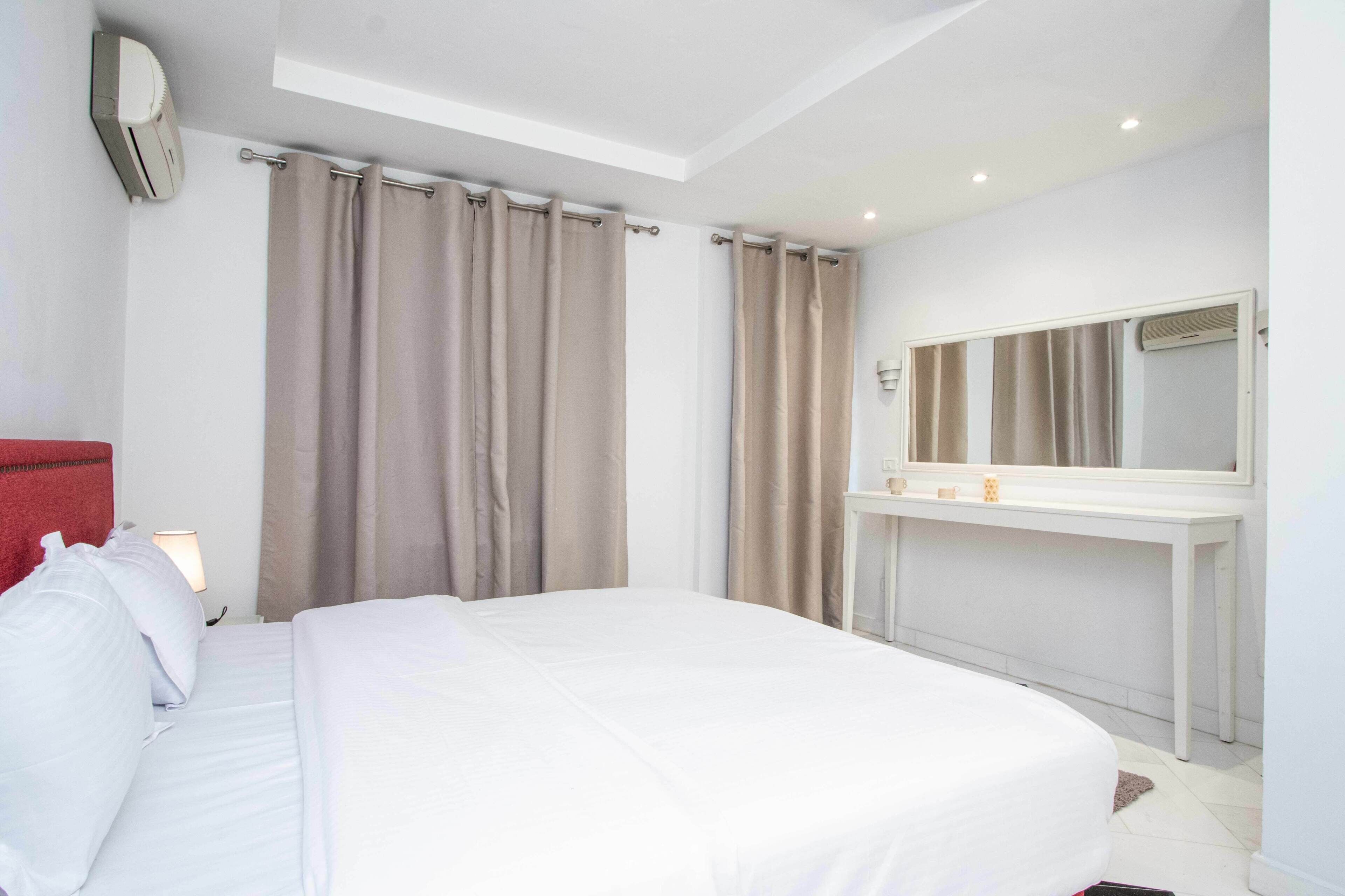A hotel room with a bed, a bedside table with a lamp, a mirror, and a wall-mounted air conditioner.