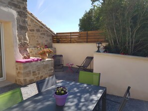 Une terrasse avec une table, des chaises, un pot de fleurs et une clĂŽture en bois.