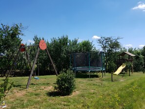 Une aire de jeux avec des balançoires, un trampoline et un toboggan.
