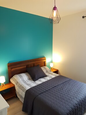 A bedroom with a teal wall, a wooden headboard, patterned bedding, and bedside lamps.