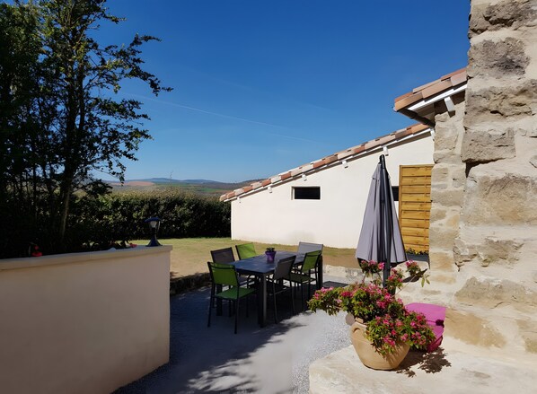 Une terrasse avec une table et des chaises, une plante en pot et un mur en pierre.