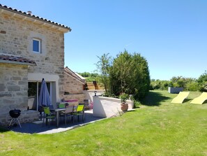 Une maison en pierre avec un patio, un espace salon extérieur et une pelouse.