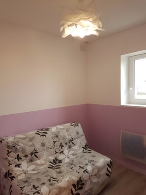 Une pièce comprenant un canapé à motifs floraux, un luminaire au plafond, une fenêtre et un radiateur.