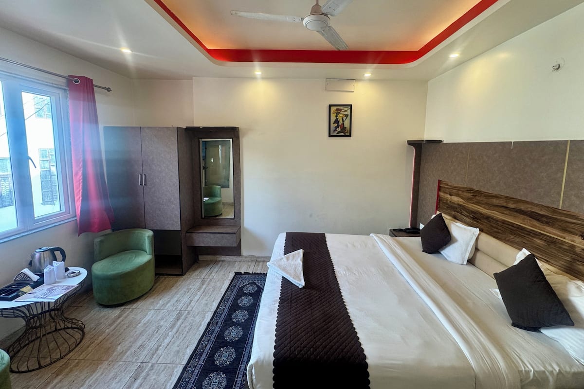 A hotel room with a bed, a desk, a chair, a window with curtains, a ceiling fan, and a painting on the wall.