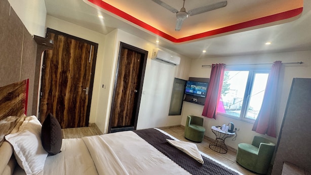 Quarto de hotel com cama, televisão, ventoinha no teto e janela com cortinas.