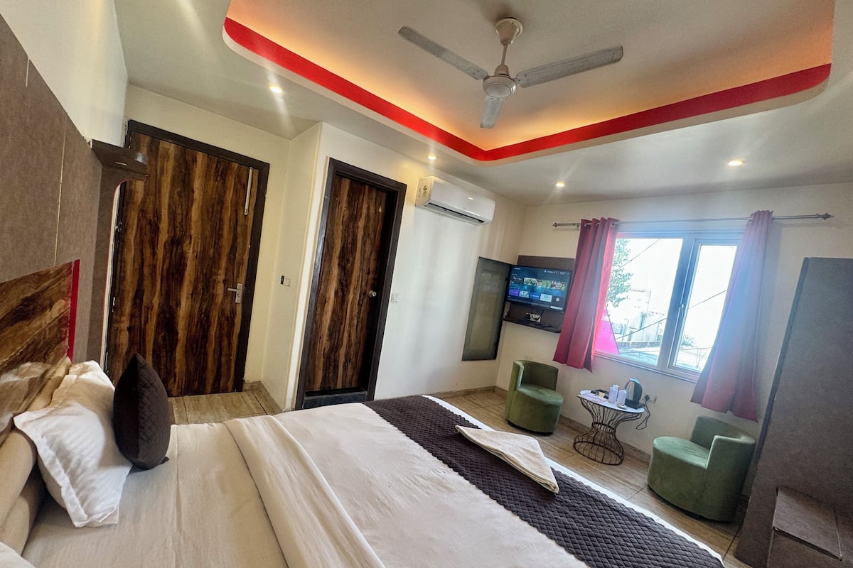 A hotel room with a bed, a TV, a ceiling fan, and a window with curtains.