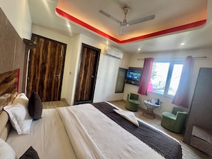 A hotel room with a bed, a TV, a ceiling fan, and a window with curtains.