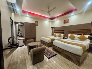 A hotel room with two beds, a sofa, a coffee maker, a mirror, and a ceiling fan.