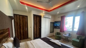 Quarto de hotel com cama, duas portas, televisão, mesinha e duas cadeiras.