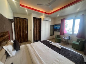 A hotel room with a bed, two doors, a TV, a small table, and two chairs.