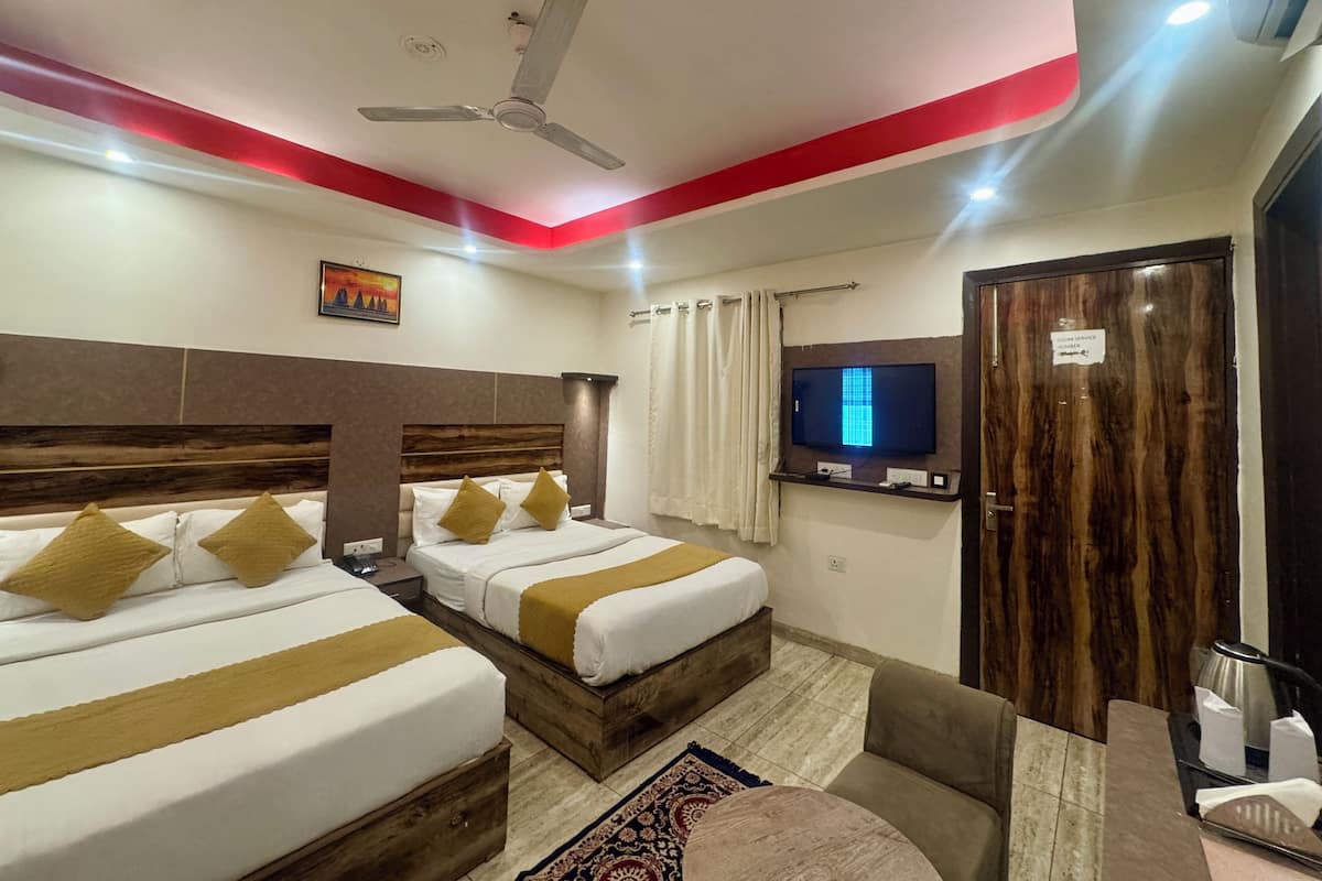 A hotel room with two beds, a ceiling fan, a TV, and a wooden door.