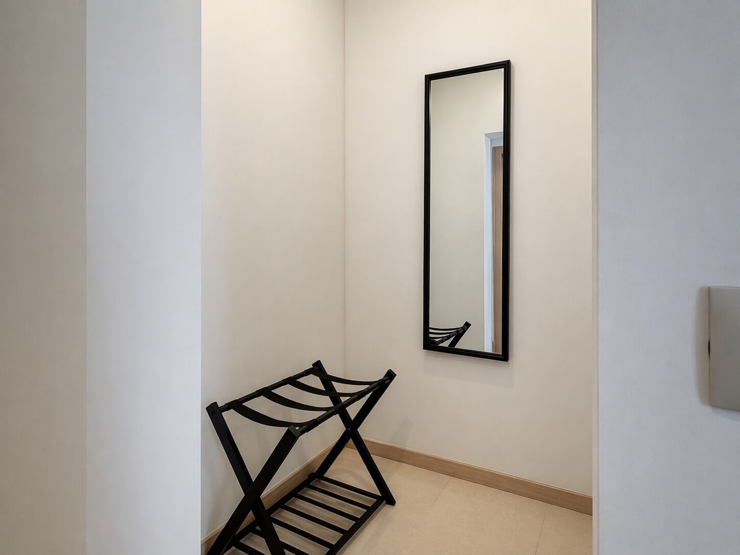 Un couloir avec un miroir, un banc en métal noir et un plancher de couleur claire.