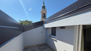 Une terrasse sur le toit offrant une vue sur le clocher d’une église, une petite fenêtre et une porte.