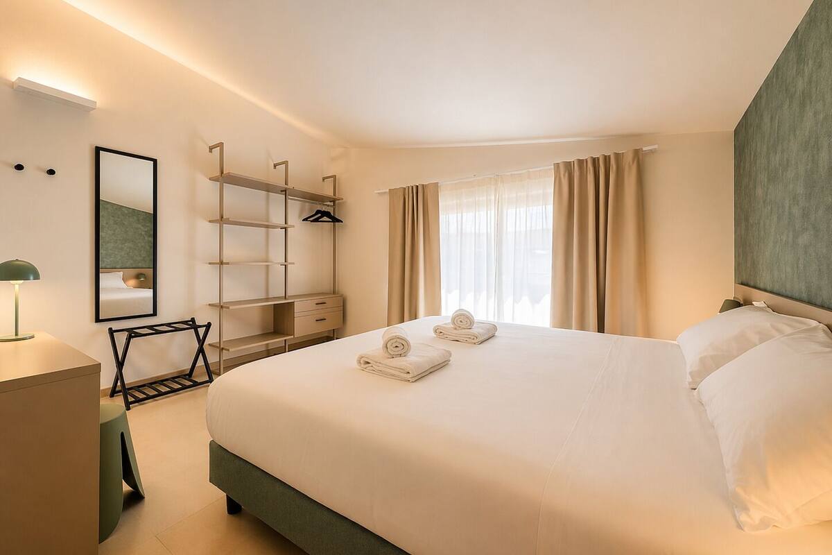 A hotel room with a large bed, a wardrobe, a desk, and a mirror.