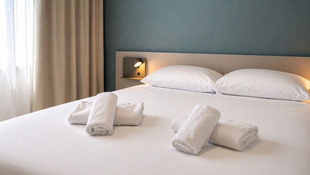 Une chambre d’hôtel avec un lit, deux oreillers, une table de chevet avec une lampe et une fenêtre avec des rideaux.