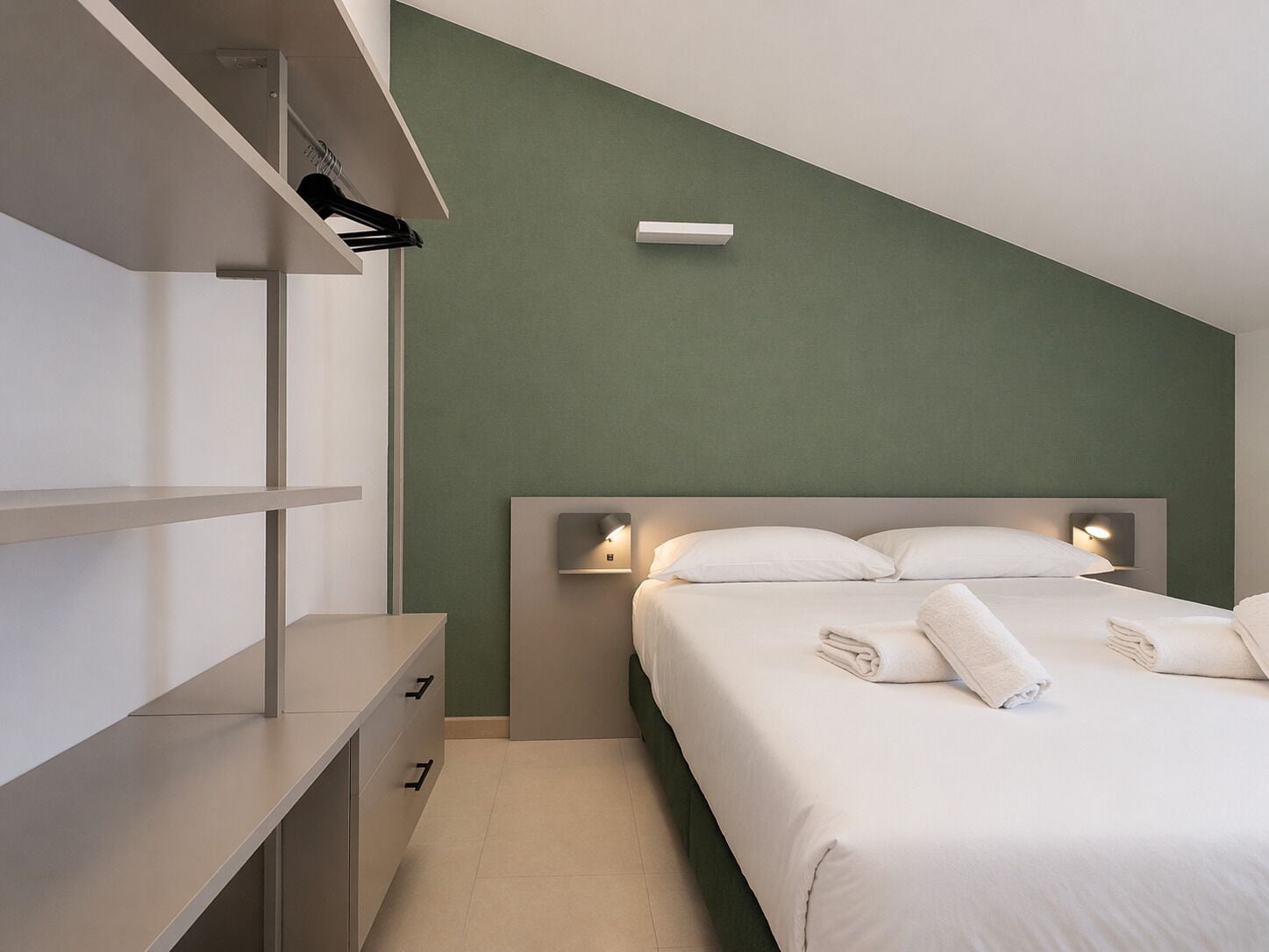 Un dormitorio con cama, mesitas de noche, armario e iluminación en la pared.