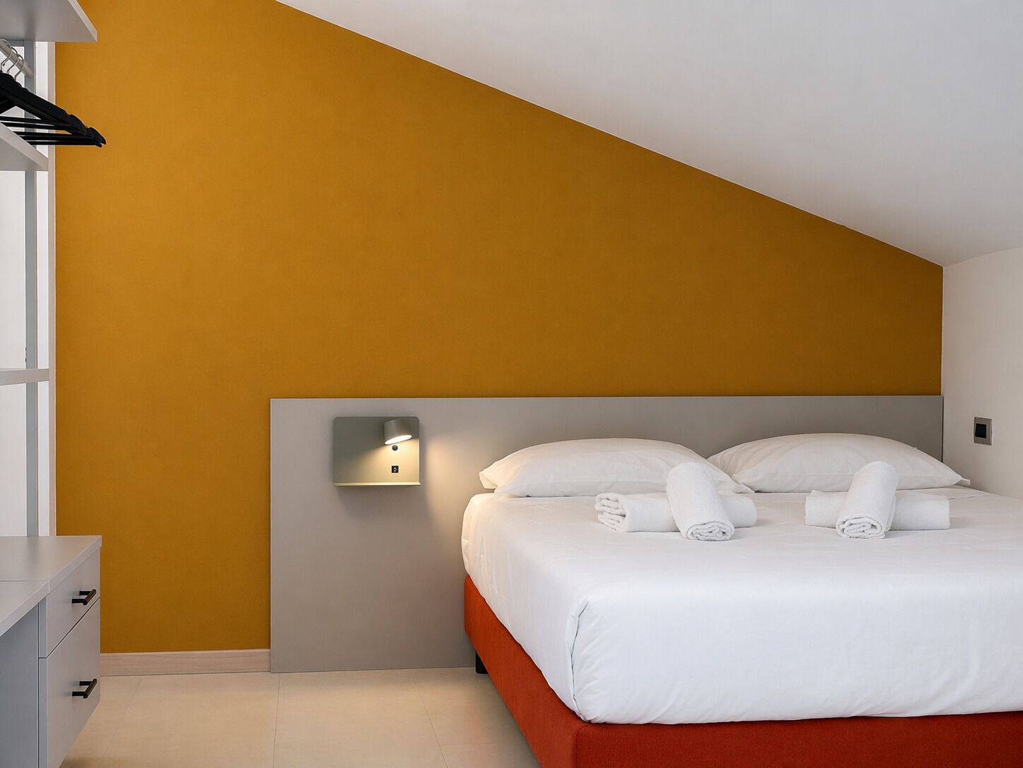 Habitació d'hotel amb llit, taulell de nit, làmpada de paret i armari.