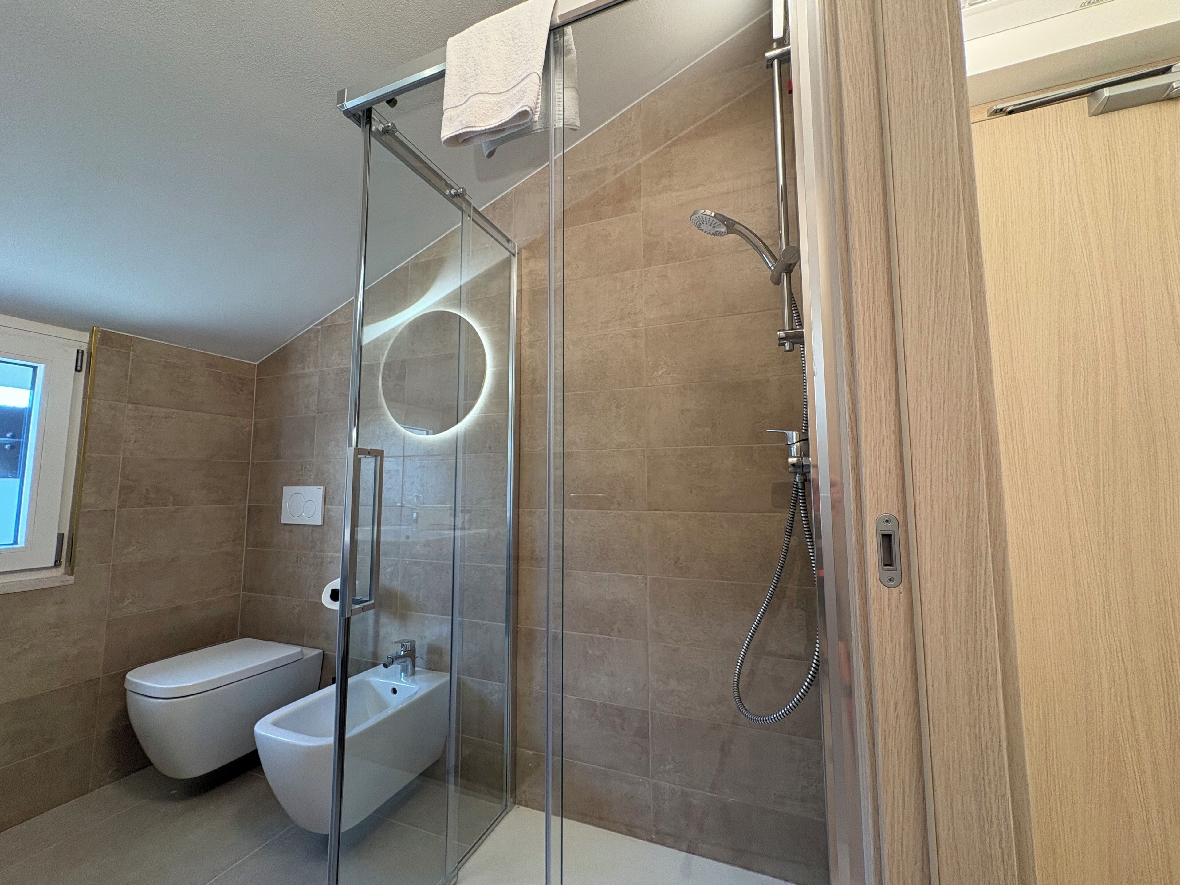 Een moderne badkamer met een douchecabine van glas, een toilet en een douchewc.