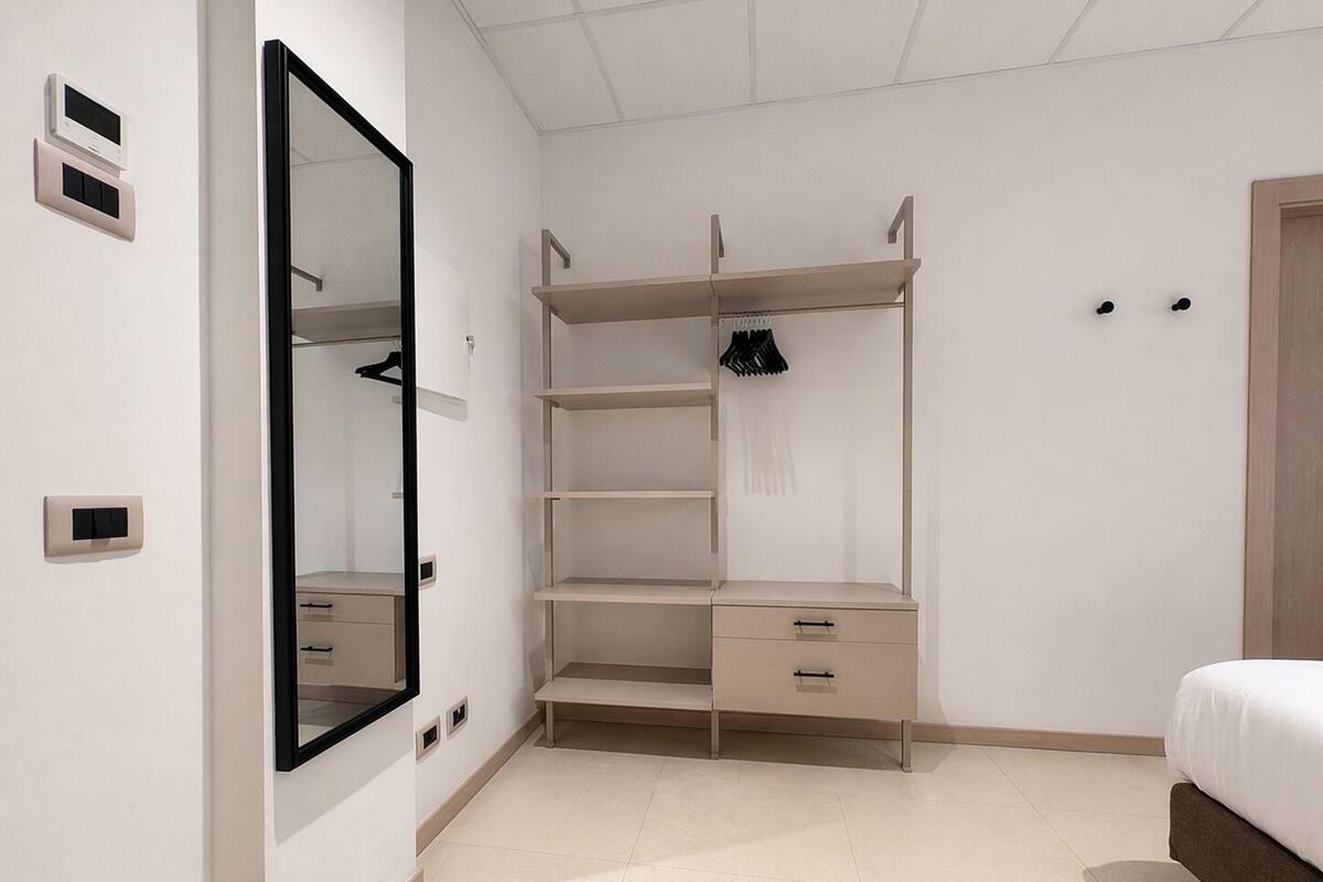A bedroom with a bed, a wardrobe with shelves, a mirror, and a door.